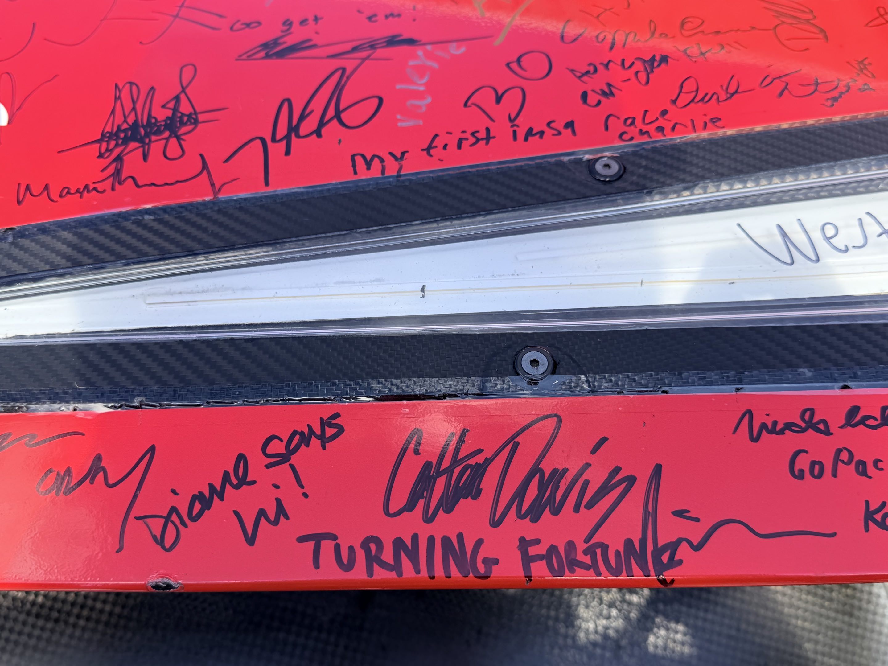 The red front clip of a race car covered in signatures, one of which says TURNING FORTUNE